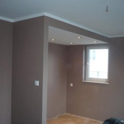Kamil Grącki - Pomieszczenie po malowaniu na kolor taupe z białymi listwami przysufitowymi i oknem; widoczne ślady po zabezpieczeniu podłogi.