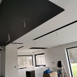 Kamil Grącki - Częściowo pomalowany sufit z czarnymi elementami dekoracyjnymi i wystającymi kablami w nowo wykończonym wnętrzu, widoczne okna i drabina.