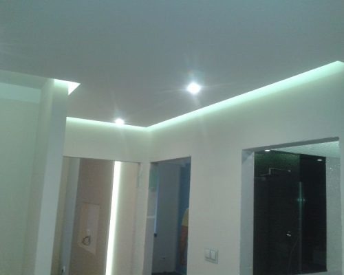 Nowoczesne wnętrze z podświetlanym sufitem, widok na dwa otwory drzwiowe i kabinę prysznicową z czarnego szkła.