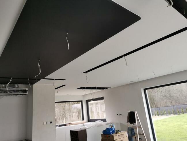 Częściowo pomalowany sufit z czarnymi elementami dekoracyjnymi i wystającymi kablami w nowo wykończonym wnętrzu, widoczne okna i drabina.