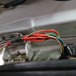 Car Serwis Sławno - Wiązka przewodów samochodowych z nowymi, czerwonymi koszulkami termokurczliwymi, zabezpieczona czarną taśmą izolacyjną, widoczna na tle metalowej karoserii pojazdu.