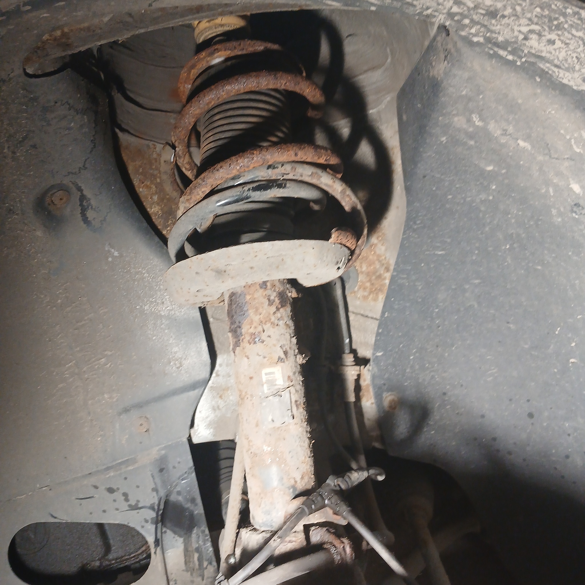 Silnie skorodowany amortyzator samochodowy z widocznymi sprężynami i elementami mocującymi, w brudnym nadkolu.