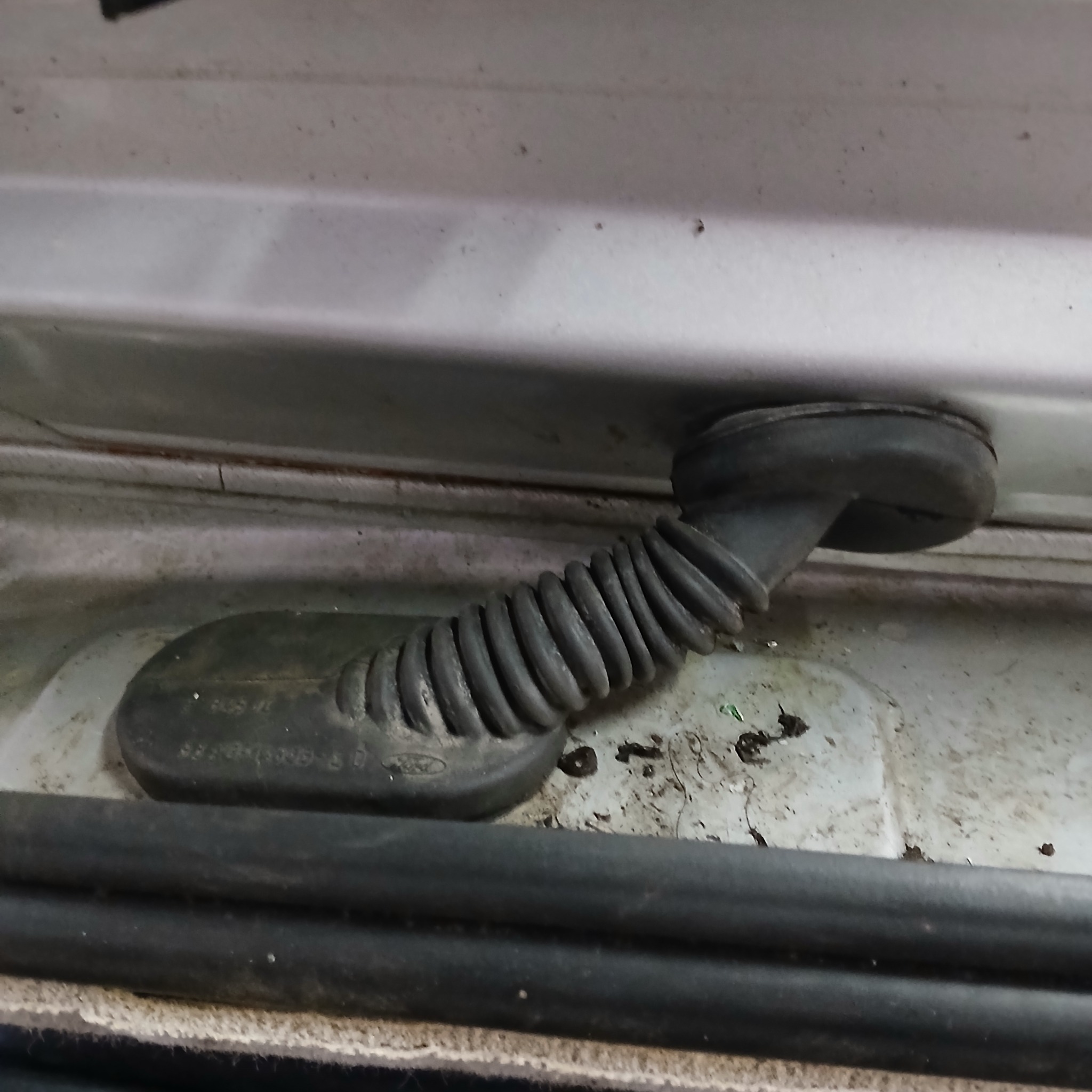 Gumowa osłona przewodów elektrycznych w karoserii samochodu marki Ford, widoczne zabrudzenia.