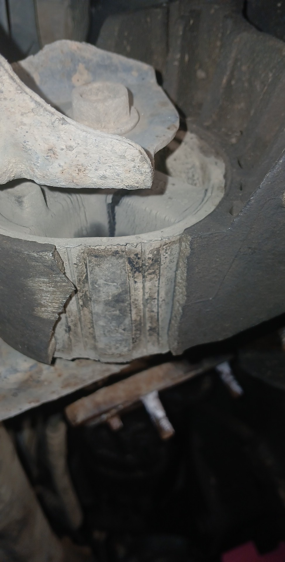 Uszkodzona, pęknięta gumowa tuleja metalowo-gumowa zawieszenia pojazdu, widoczne ślady korozji i zabrudzenia.