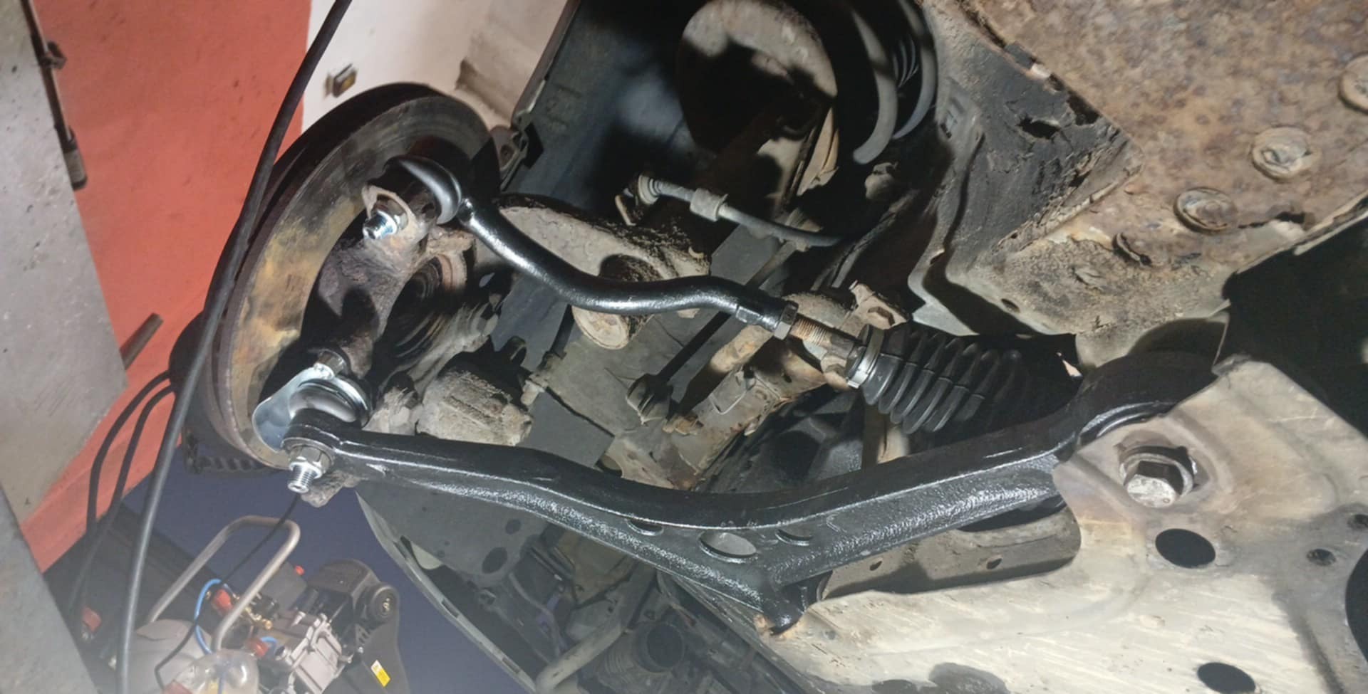 Zawieszenie samochodu w trakcie naprawy, widoczne elementy układu kierowniczego po konserwacji, z widocznymi śladami korozji na elementach konstrukcyjnych podwozia.