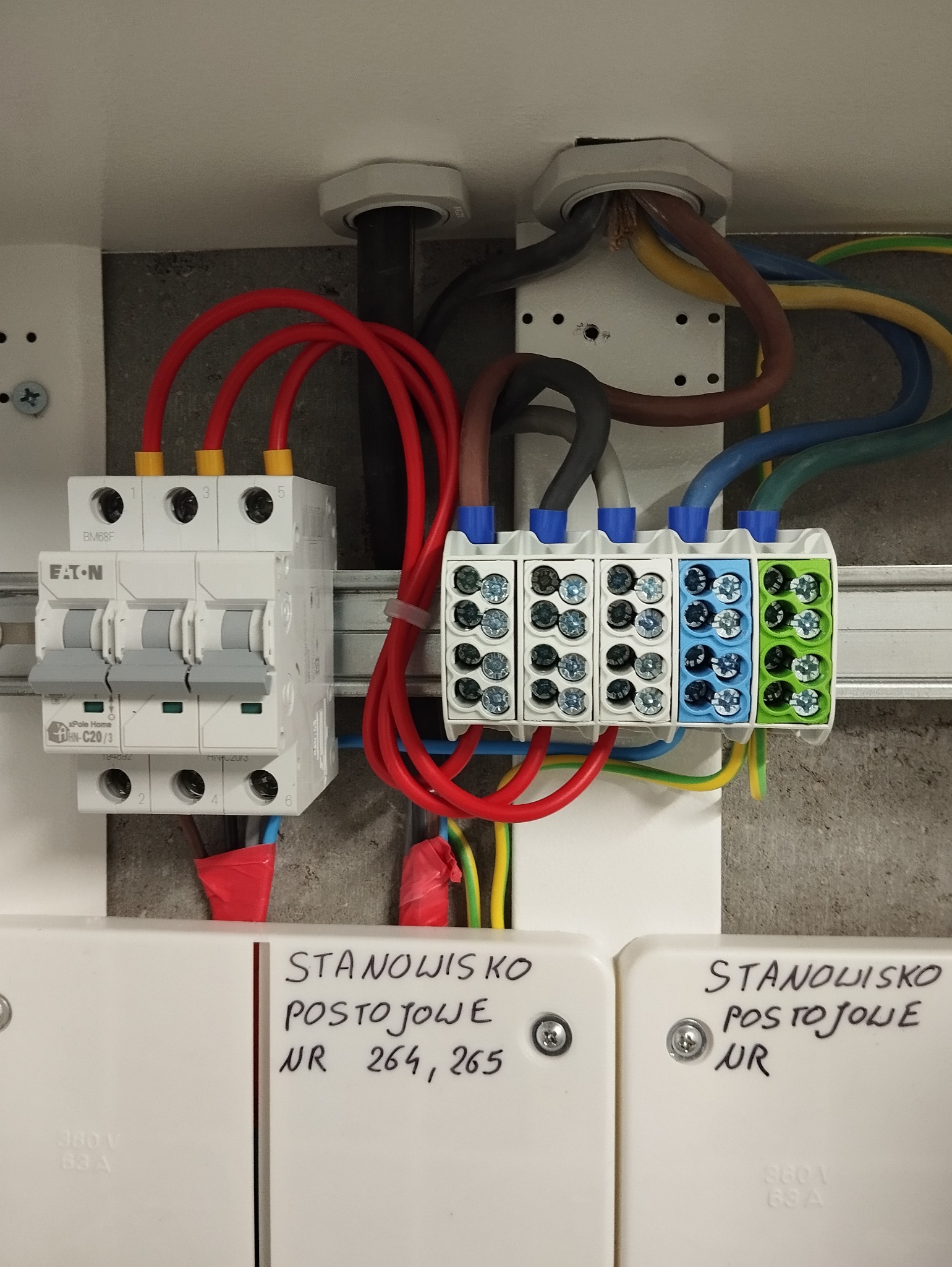 Szczegółowe ujęcie skrzynki elektrycznej z zainstalowanymi bezpiecznikami Eaton i listwami zaciskowymi z kolorowymi oznaczeniami przewodów, widoczne napisy 'Stanowisko postojowe NR 264, 265'...