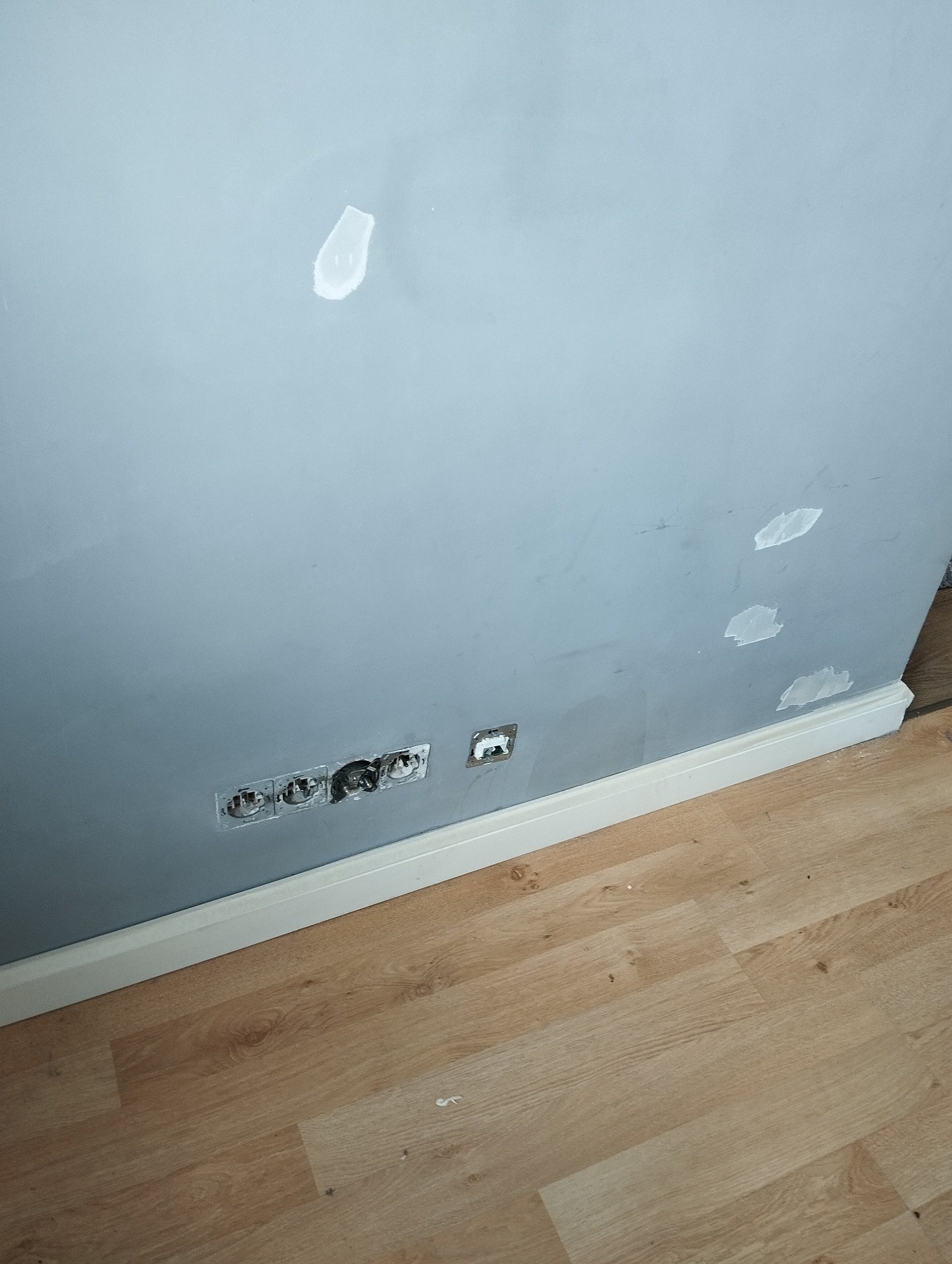 Przygotowanie ściany do malowania w Warszawie: szpachlowane ubytki i gniazdka elektryczne bez osprzętu, listwa przypodłogowa, podłoga laminowana.