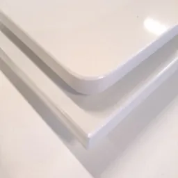 Dwa białe blaty z konglomeratu kwarcowego, jeden z zaokrąglonym narożnikiem, ułożone jeden na drugim, widoczne z bliska w neutralnym oświetleniu.