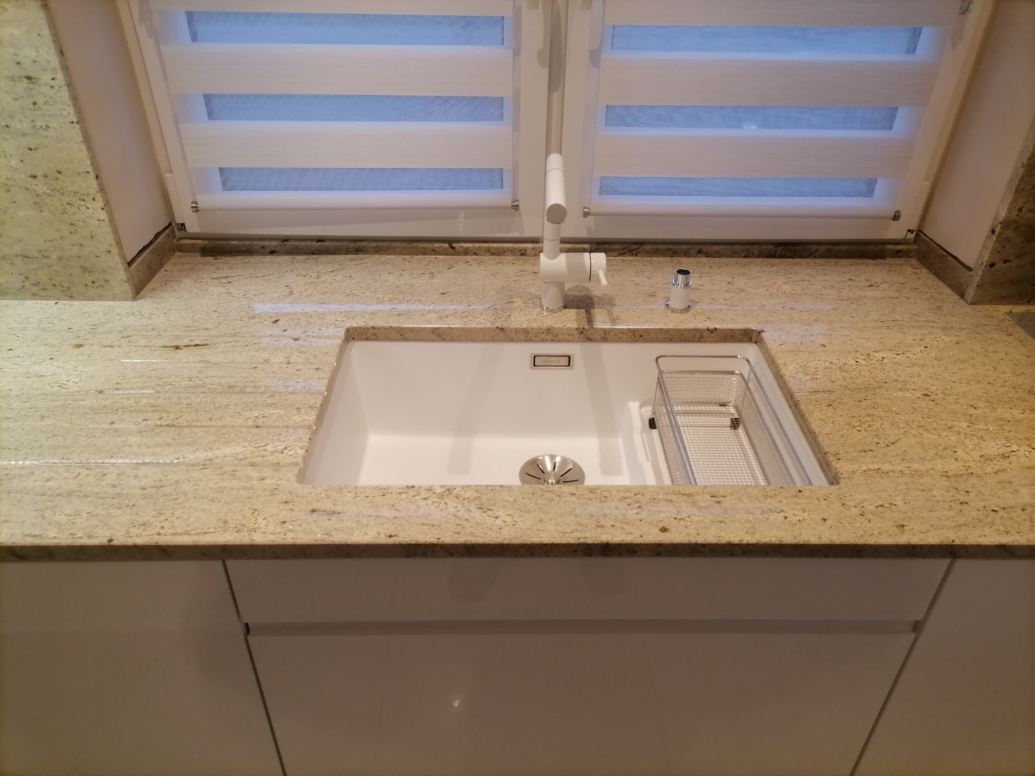 Jasny blat kuchenny z konglomeratu z wbudowanym białym zlewem i metalową suszarką, widok z przodu, biała bateria i dozownik płynu.