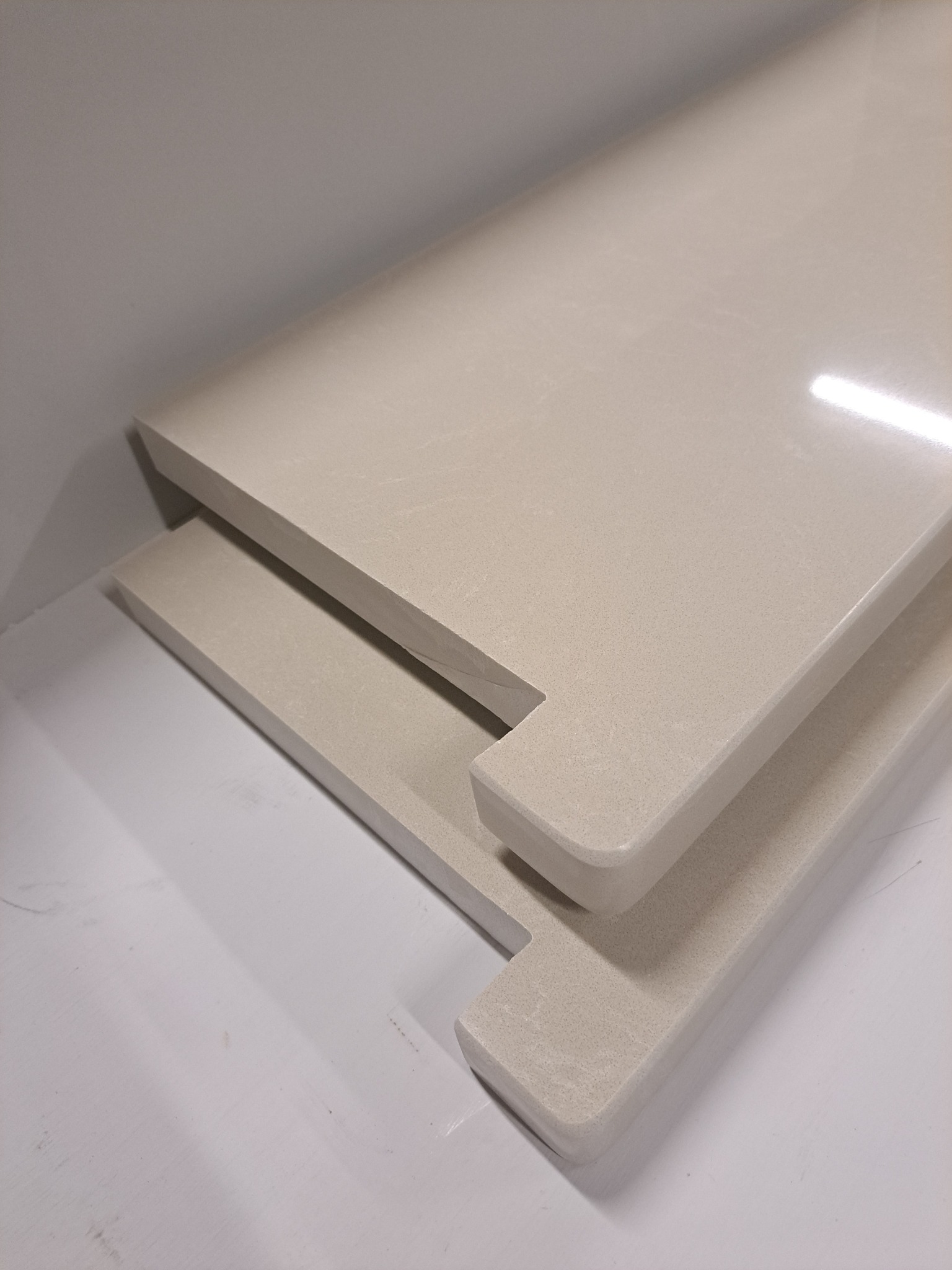 Dwa elementy z beżowego konglomeratu z wycięciami, leżące jeden na drugim w magazynie lub warsztacie.