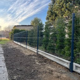 TYMACOMPANY SPÓŁKA Z OGRANICZONĄ ODPOWIEDZIALNOŚCIĄ - Nowoczesne ogrodzenie panelowe z podmurówką betonową, widok z boku na tle zielonych drzew i błękitnego nieba z chmurami.