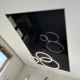 PerfectFinish - Czarny, lustrzany sufit z podwieszonymi, okrągłymi lampami LED w pomieszczeniu w trakcie wykańczania, widoczne ślady po gładzi na ścianach i okno dachowe.