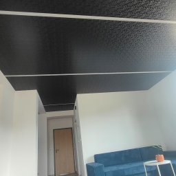 PerfectFinish - Czarne, wzorzyste sufity w salonie z niebieską sofą i stolikiem kawowym, widok z dołu, jasne ściany.