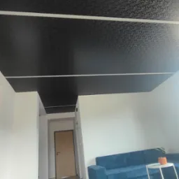 Czarne, wzorzyste sufity w salonie z niebieską sofą i stolikiem kawowym, widok z dołu, jasne ściany.