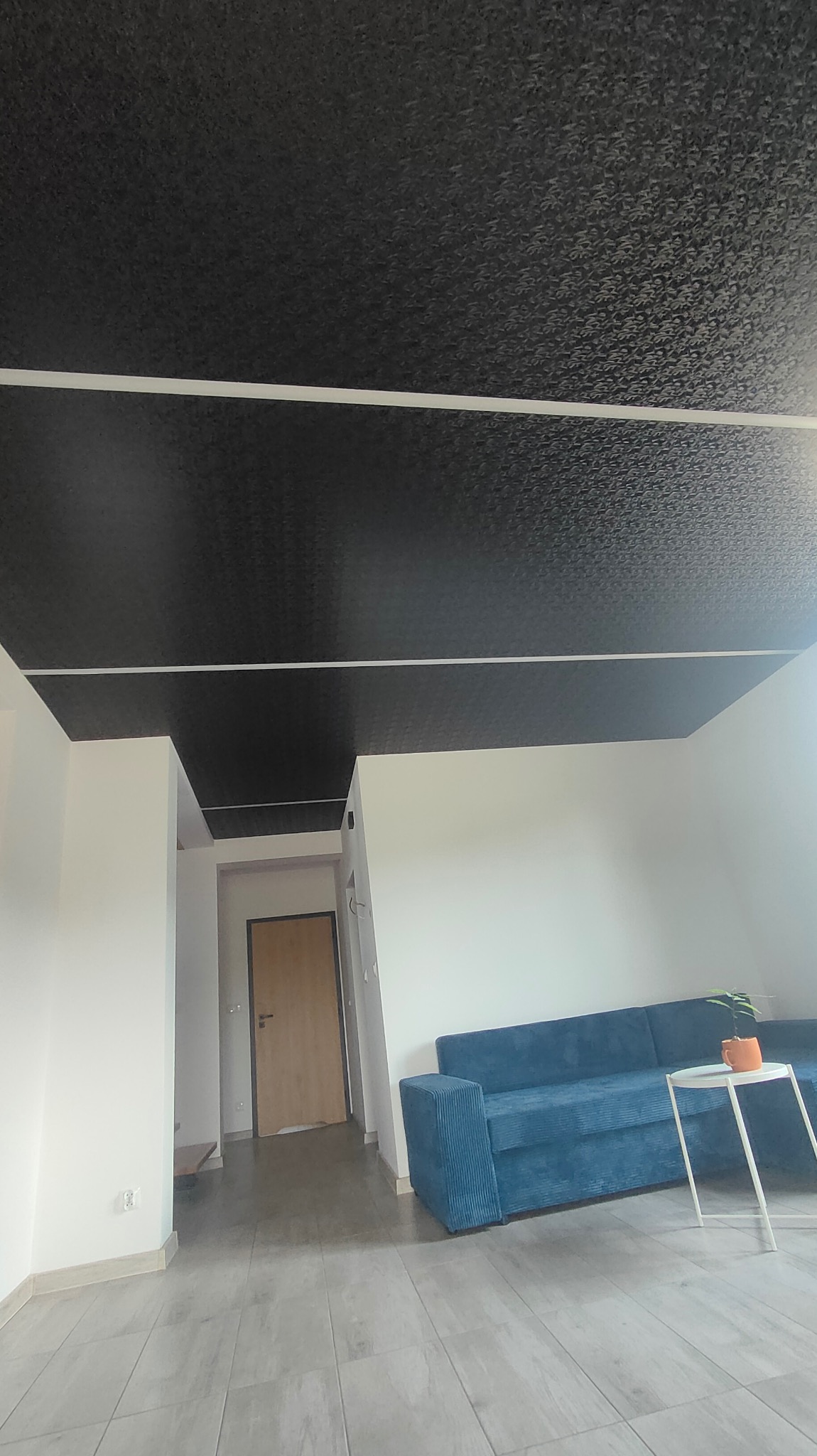 Czarne, wzorzyste sufity w salonie z niebieską sofą i stolikiem kawowym, widok z dołu, jasne ściany.