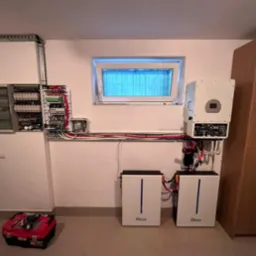 Wnętrze pomieszczenia z zainstalowanym systemem fotowoltaicznym: skrzynka rozdzielcza, falownik i dwa akumulatory Deye, widoczna skrzynka narzędziowa.