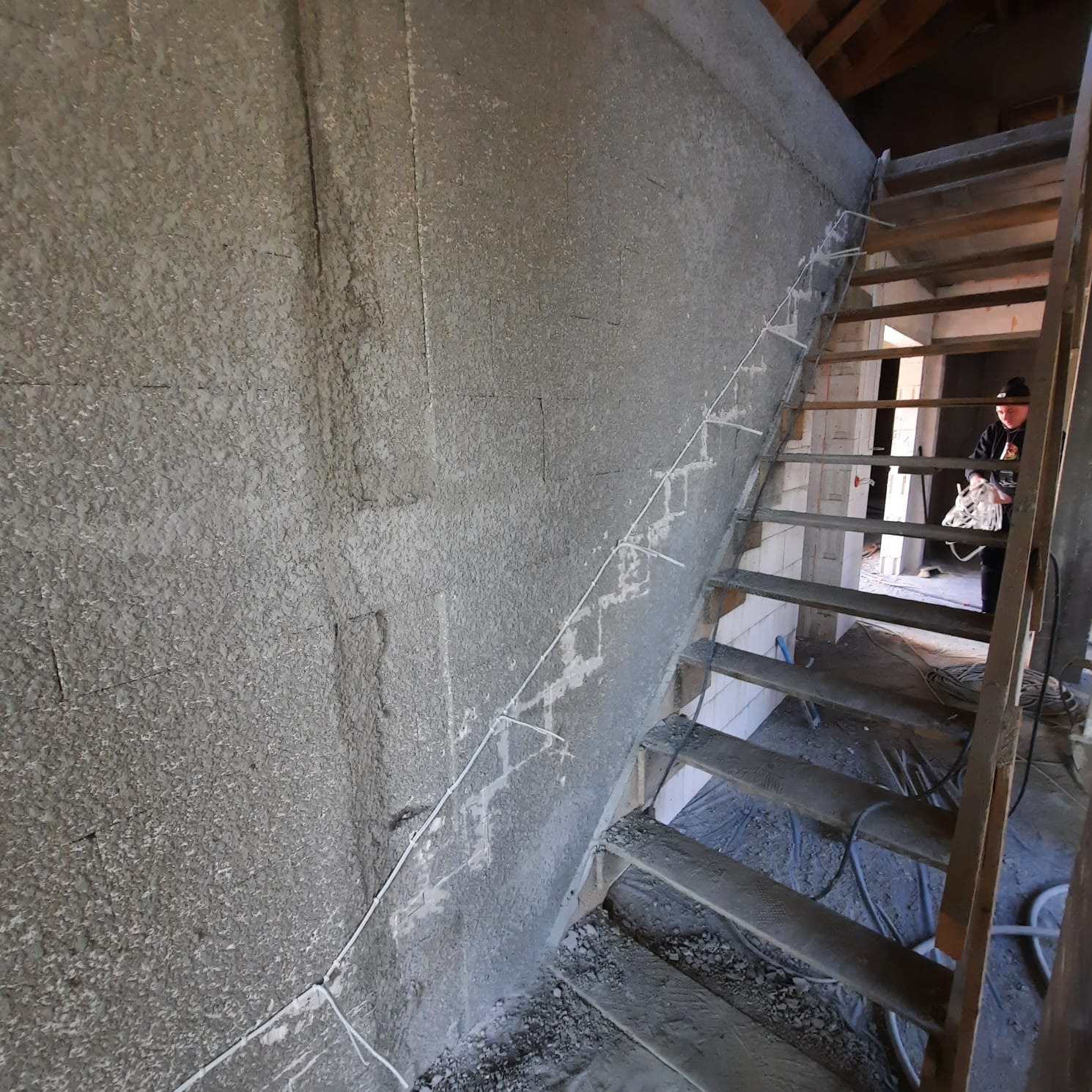 Przygotowanie trasy kablowej na surowej ścianie wzdłuż drewnianych schodów w trakcie prac wykończeniowych.