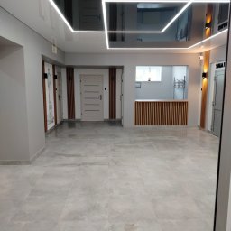 KAMIL NIEDZIELSKI KN-BUD - Wykończone wnętrze biura z błyszczącym sufitem, oświetleniem LED, szarymi ścianami, drewnianymi panelami i jasnymi płytkami podłogowymi. Widok na recepcję.