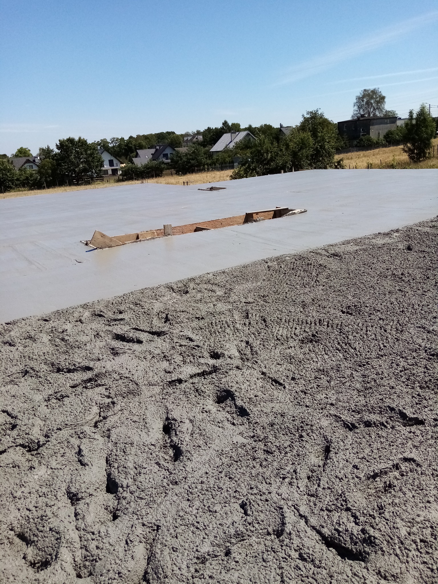 Wylany fundament pod budowę domu w Rybniku, widoczne ślady butów na świeżym betonie i drewniane szalunki.