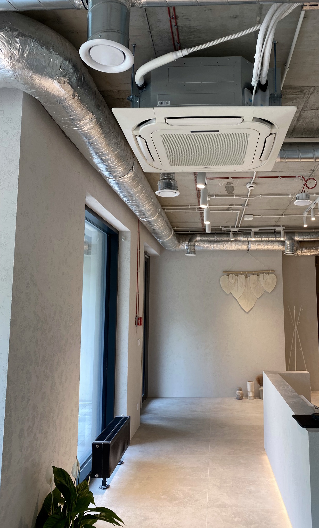 Nowoczesne wnętrze biurowe z zainstalowanym sufitem kasetonowym z klimatyzatorem AUX, widoczne kanały wentylacyjne, oświetlenie punktowe i minimalistyczny wystrój.