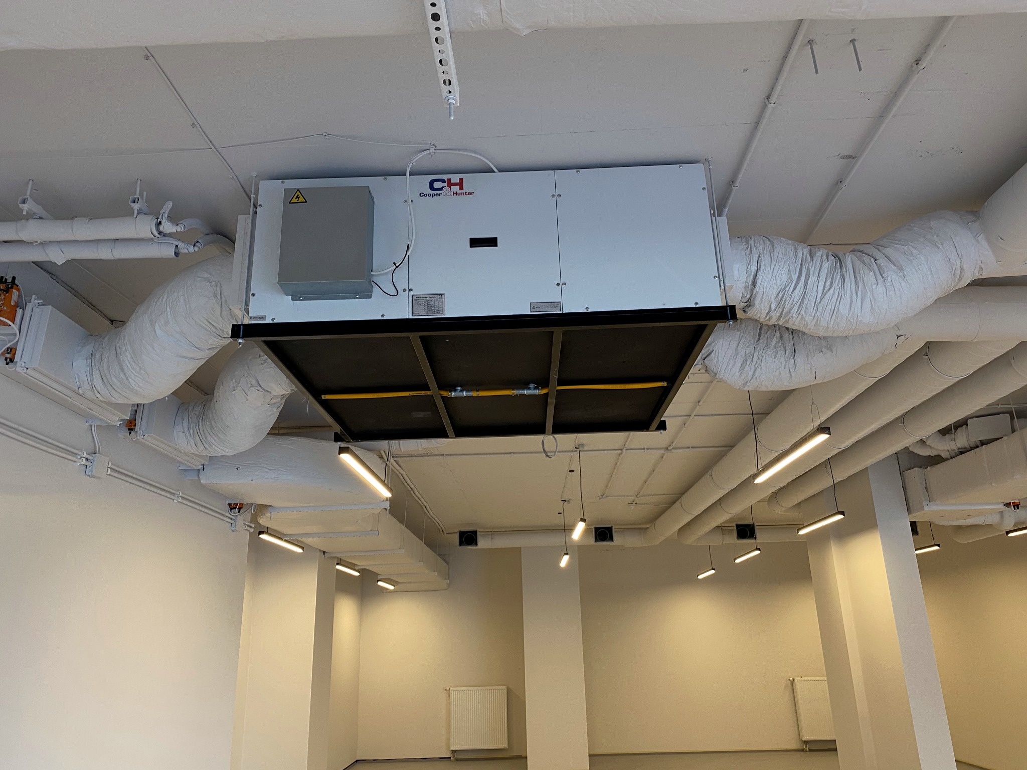 Instalacja wentylacyjna Cooper&Hunter z kanałami powietrznymi w przestrzeni komercyjnej, widok z dołu na sufit z oświetleniem liniowym.