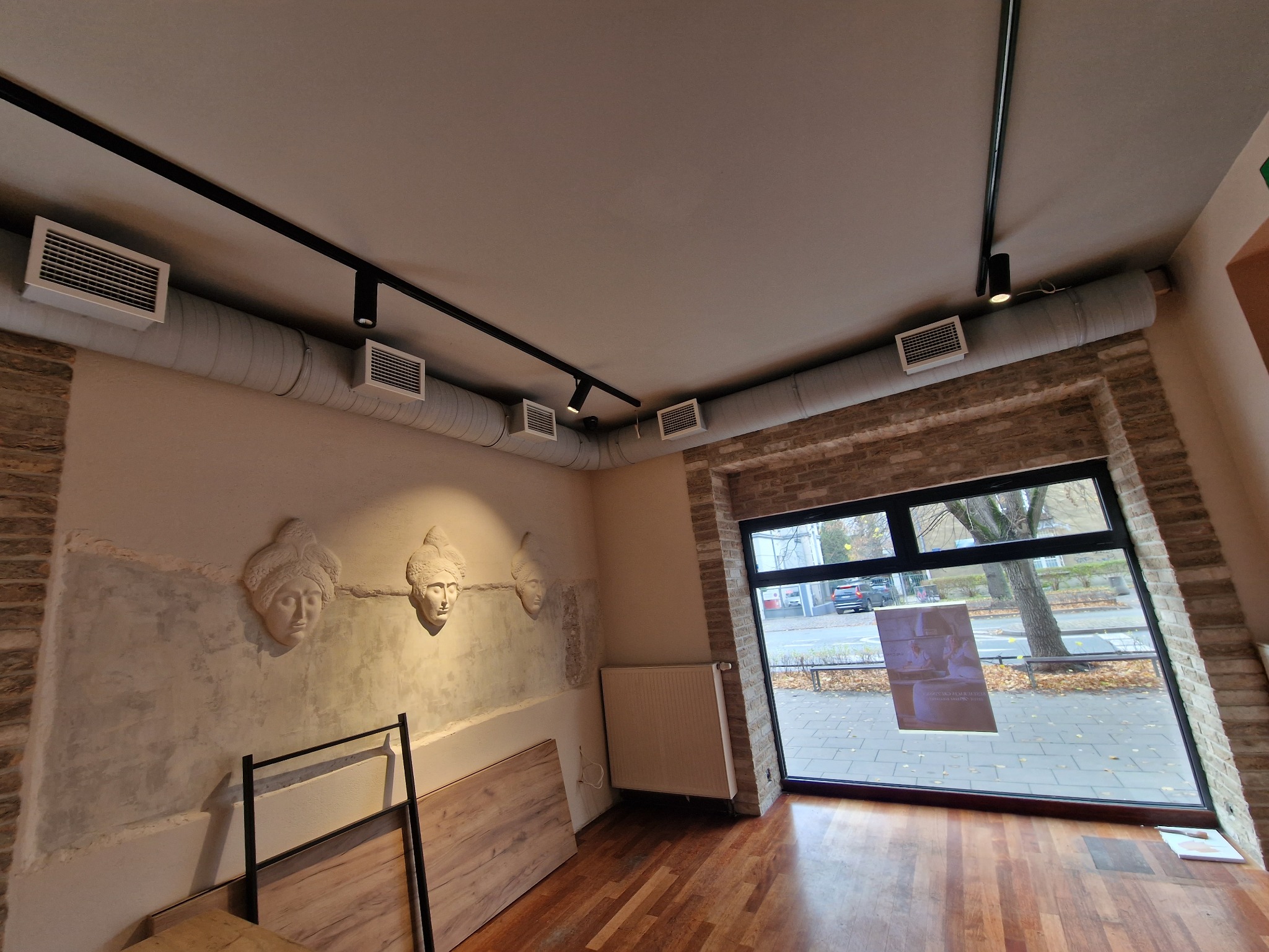 Wnętrze lokalu w Gdańsku z widocznymi elementami wentylacji pod sufitem, listwami oświetleniowymi, dekoracyjnymi płaskorzeźbami na ścianie i dużym oknem z widokiem na ulicę.