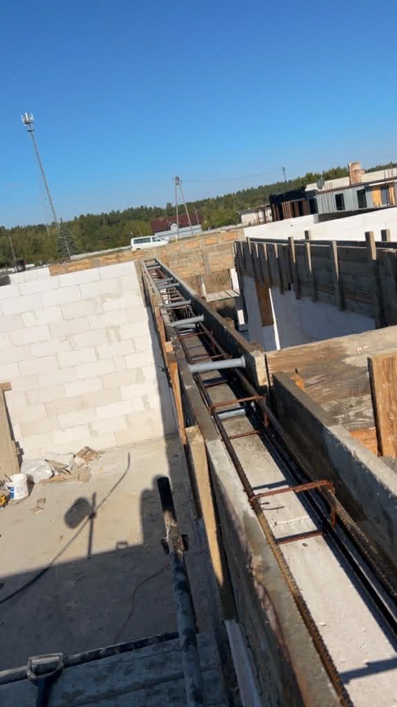 Zbrojenie fundamentów domu z bloczków betonowych, widok z góry na szalunek z ułożonymi prętami zbrojeniowymi i elementami dystansowymi. Budowa w słoneczny dzień.