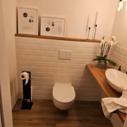 Nowoczesna łazienka z drewnianą podłogą i blatem, białą armaturą, płytkami typu metro oraz dekoracjami: ramki, świece i orchidea.