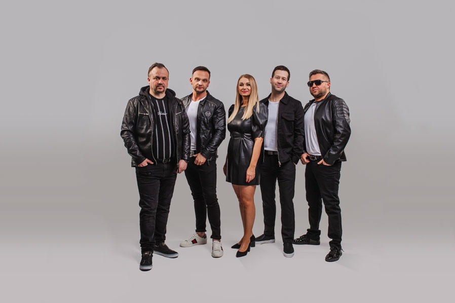 Zespół muzyczny w skórzanych kurtkach, pozujący na jasnoszarym tle. Wokalistka w czarnej sukience pośrodku. Męska część zespołu w czarnych spodniach i koszulach.