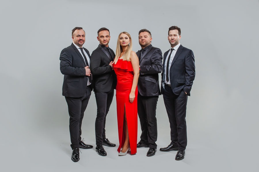 Zespół muzyczny: czterech mężczyzn w czarnych garniturach i kobieta w czerwonej sukni wieczorowej, pozują na jasnym tle. Elegancki i profesjonalny wygląd.