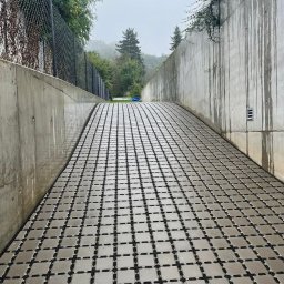 CITY BUD - Ułożona kostka na rampie w betonowym tunelu, widok w perspektywie z lekkim nachyleniem, drzewa w tle.