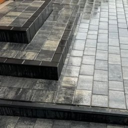 CITY BUD - Ułożone schody z kostki brukowej w odcieniach szarości, z czarnymi obrzeżami, prowadzące do budynku o brązowej elewacji.