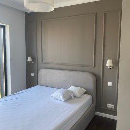 SERHII - BUD SERHII PINKO - Elegancka sypialnia w stonowanych szarościach i brązach. Dekoracyjne listwy na ścianach, minimalistyczne lampy ścienne i sufitowa. Podłoga z ciemnego drewna.