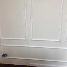 SERHII - BUD SERHII PINKO - Ściana z dekoracyjnymi panelami ściennymi w stylu klasycznym, z widocznymi puszkami elektrycznymi i podłogą. Częściowo widoczny materiał budowlany pod folią.