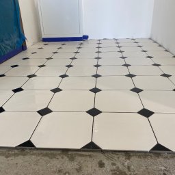 SERHII - BUD SERHII PINKO - Biało-czarna podłoga z płytek ułożonych w romby, widok z góry, świeżo po ułożeniu, z widocznymi zabezpieczeniami przy ścianie i fragmentem surowej podłogi.