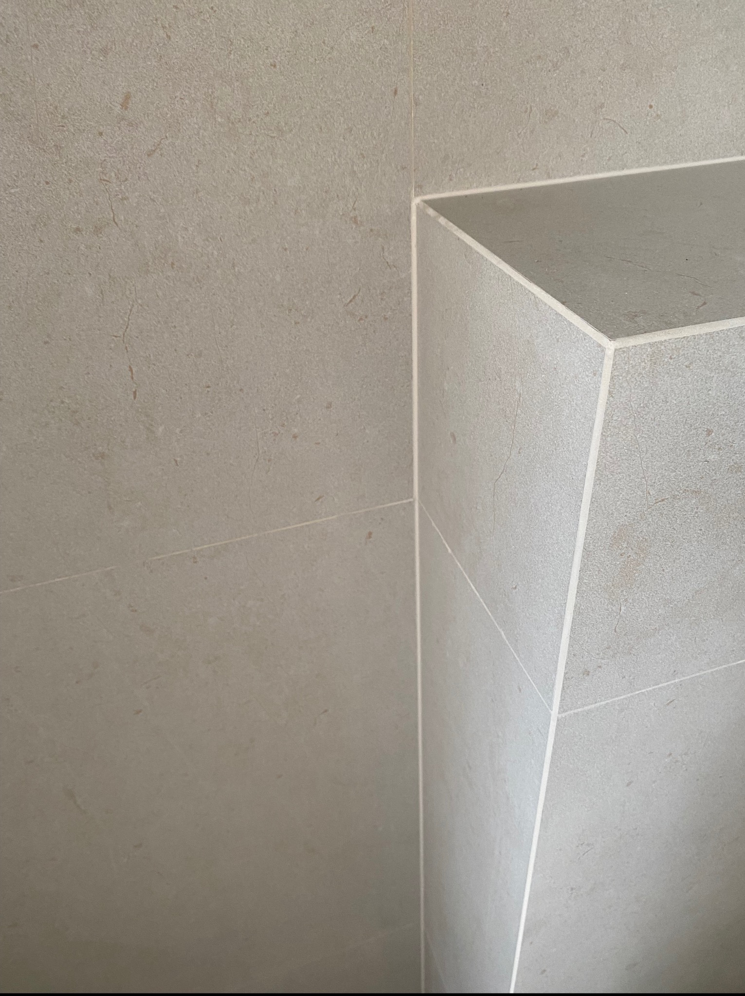 Beżowe płytki ceramiczne ułożone na ścianie i wnęce, z widocznymi fugami. Minimalistyczny design, neutralna kolorystyka i precyzyjne wykończenie.