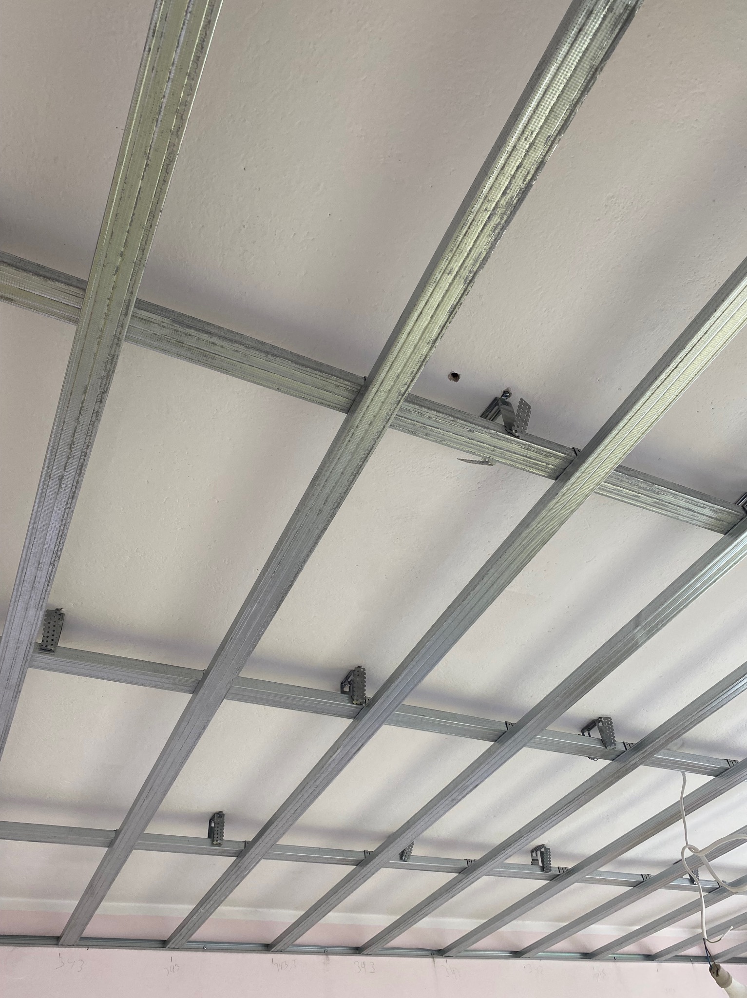 Metalowa konstrukcja sufitu podwieszanego, widok z dołu, szkielet z profili, biała powierzchnia sufitu, oświetlenie w rogu kadru.