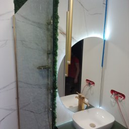 Detailo Craft - Nowoczesna łazienka w trakcie wykańczania: kabina prysznicowa z zielonym mchem, okrągłe lustro z podświetleniem LED, biała umywalka nablatowa z złotą armaturą, widoczne niepodłączone przewody...