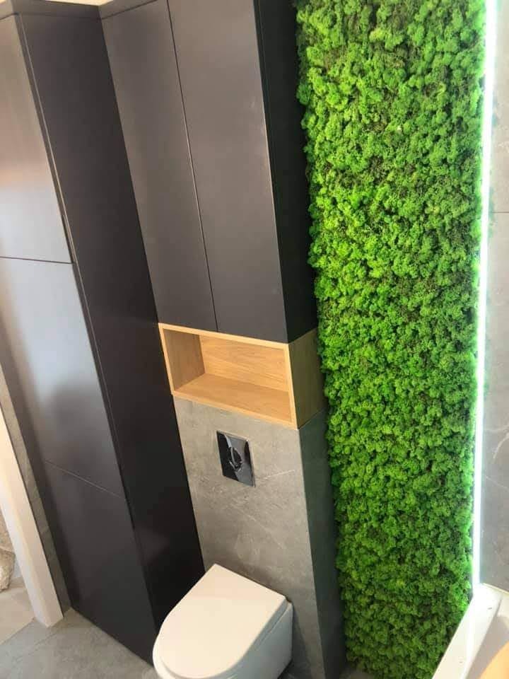 Nowoczesna łazienka z toaletą podwieszaną, zabudową szafek w kolorze antracytowym, drewnianą półką i pionowym panelem z mchu chrobotka podświetlonym LED.
