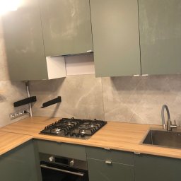 “Ręce Mistrza” usługi remontowe Anton Velychko - Nowoczesna kuchnia z frontami w odcieniach zieleni, drewniany blat, płyta gazowa i marmurowe płytki na ścianie.