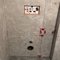 “Ręce Mistrza” usługi remontowe Anton Velychko - Montaż szarych płytek w łazience, widoczne otwory na instalacje, poziomica laserowa, krzyżyki dystansowe i elementy instalacji podtynkowej.