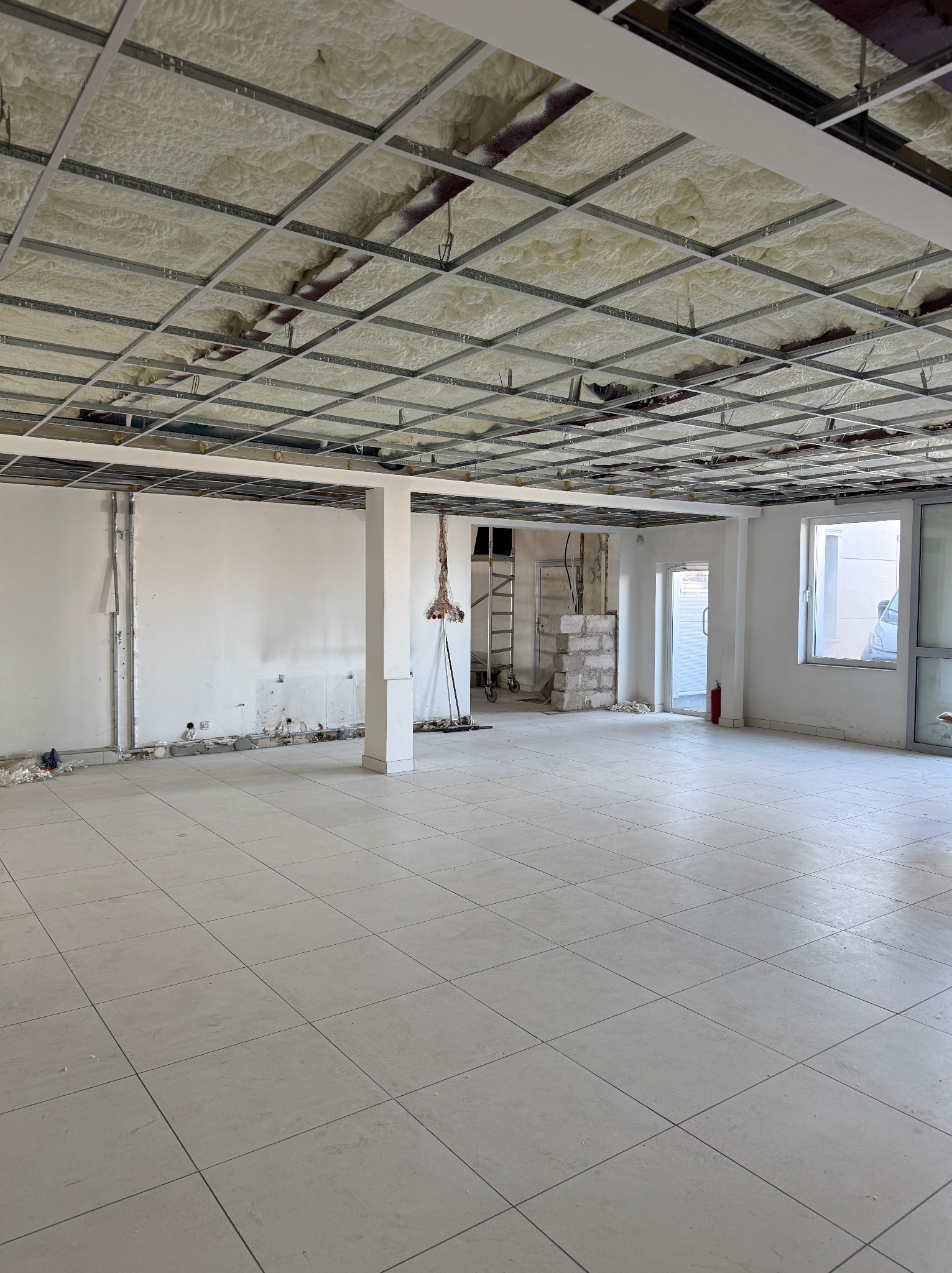 Sufit budynku komercyjnego w trakcie ocieplania pianką PUR, widoczne elementy konstrukcyjne i równomiernie nałożona warstwa izolacji, w tle ściany w stanie surowym i okno.