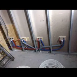 Wewnętrzne instalacje wodne i grzewcze w trakcie montażu w budynku, widoczne rury z tworzywa w kolorach niebieskim i czerwonym, częściowo ukryte w ścianie z płyt gipsowo-kartonowych na metalowym...