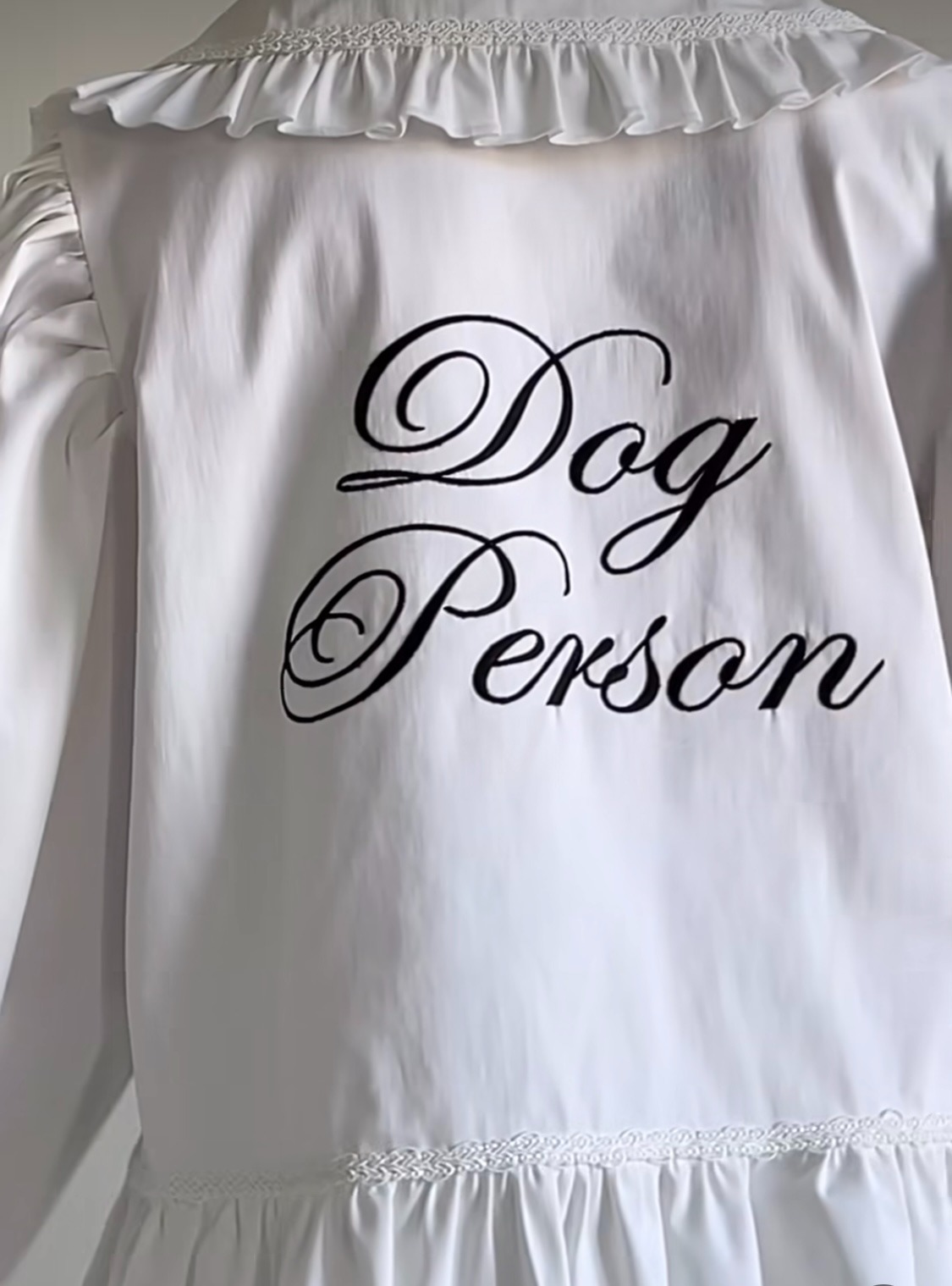 Biała bluzka z długim rękawem, zdobiona falbankami i haftowanym napisem 'Dog Person' na plecach, widok z tyłu.