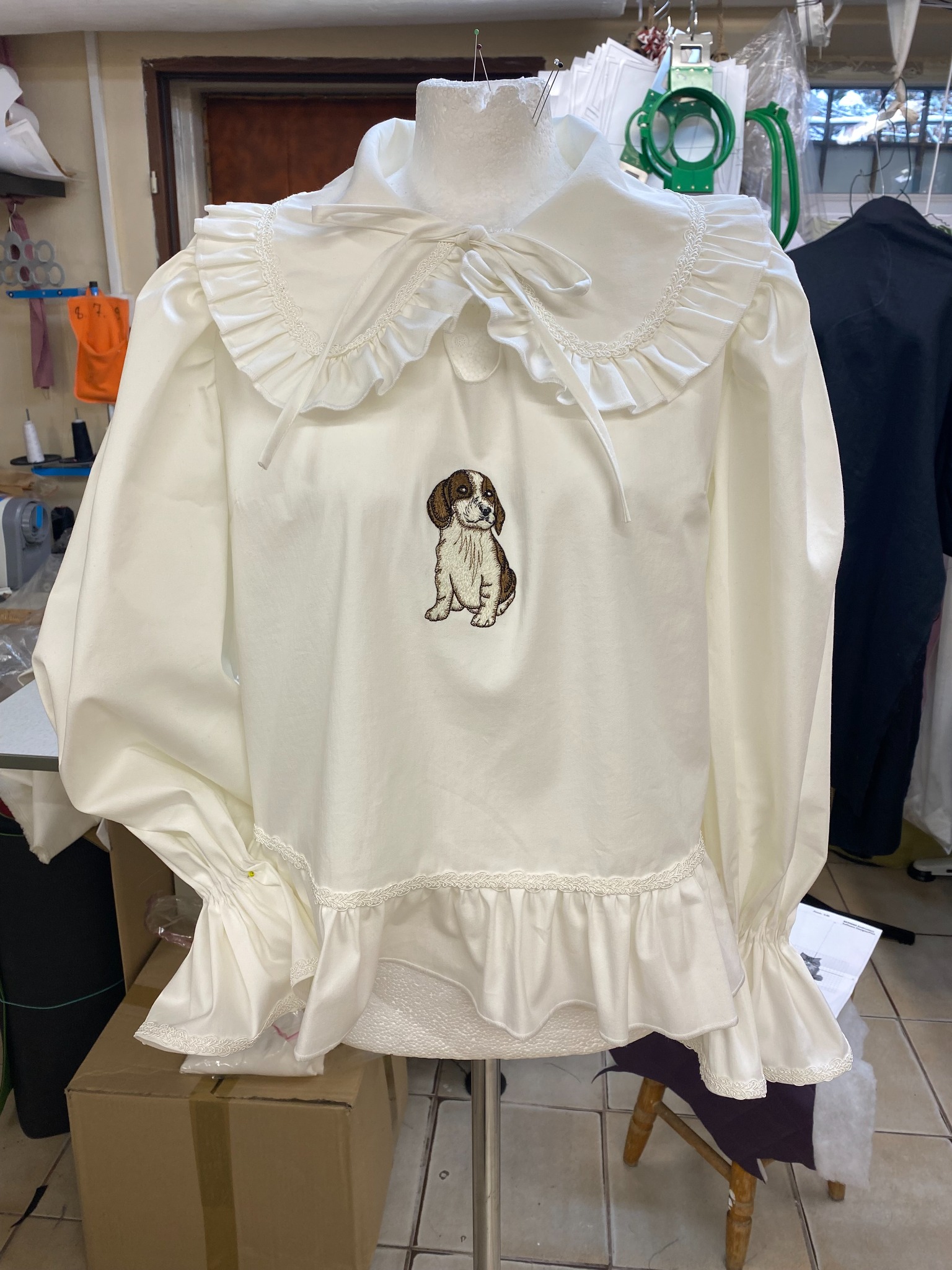 Biała bluzka damska z bufiastymi rękawami, koronkowym wykończeniem i haftem przedstawiającym szczeniaka na środku, prezentowana na manekinie.