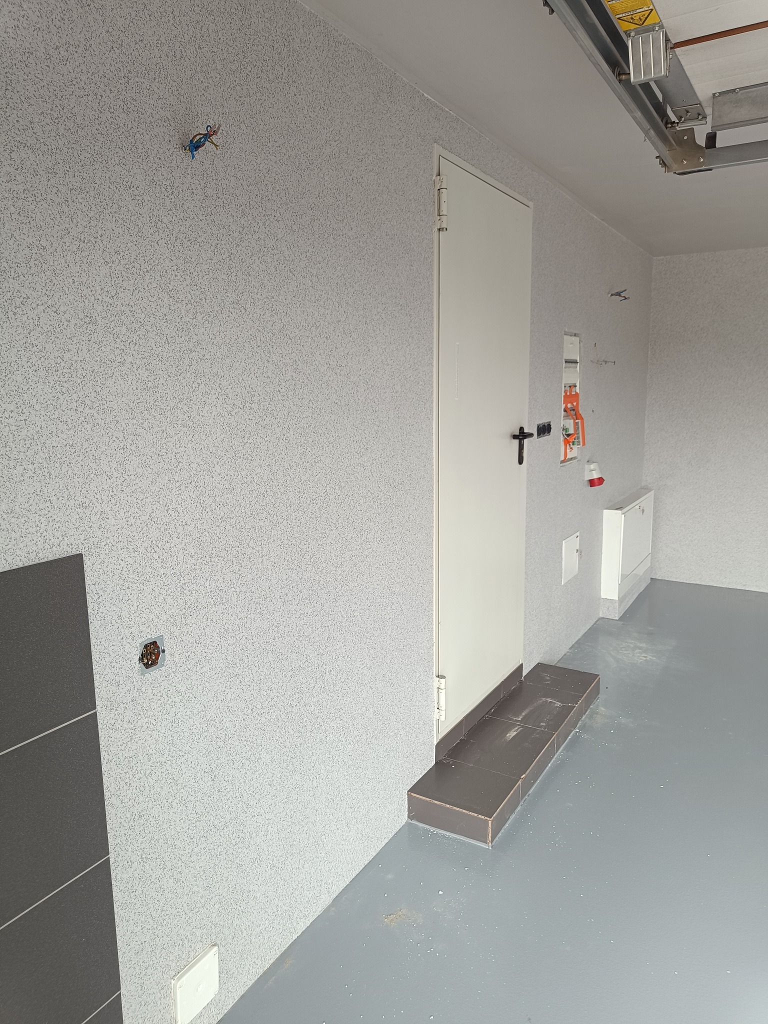 Wnętrze po remoncie w Złotnikach Kujawskich: ściany z fakturą, gładka, szara podłoga, białe drzwi i widoczna instalacja elektryczna. Elementy wykończeniowe.