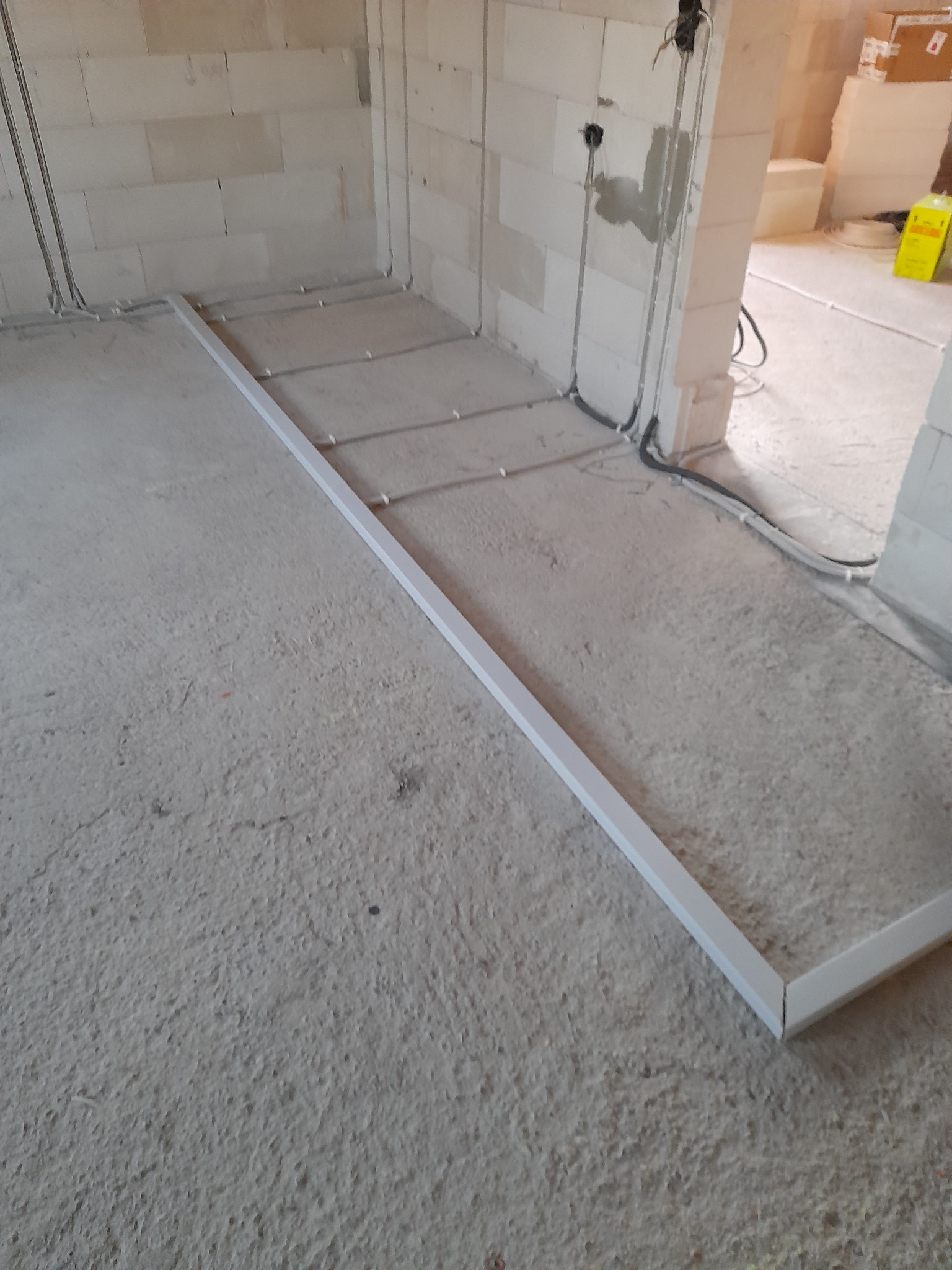 Surowy stan podłoża w trakcie prac instalacyjnych, widoczne kable elektryczne prowadzone po podłodze, przygotowane pod wylewkę, biała listwa przyścienna.