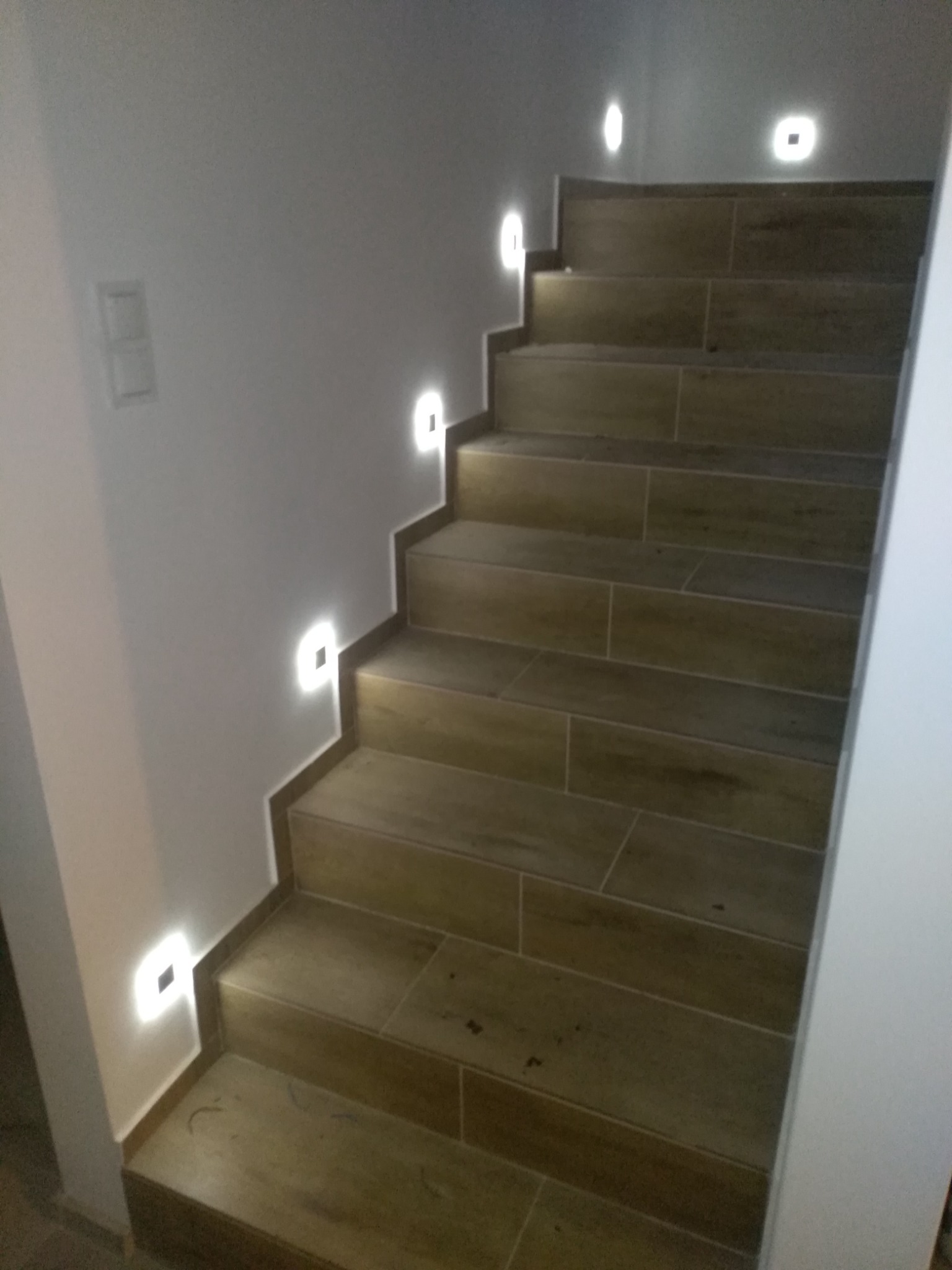 Schody wyłożone płytkami imitującymi drewno z zainstalowanym oświetleniem punktowym LED w ścianie, widok z dołu.