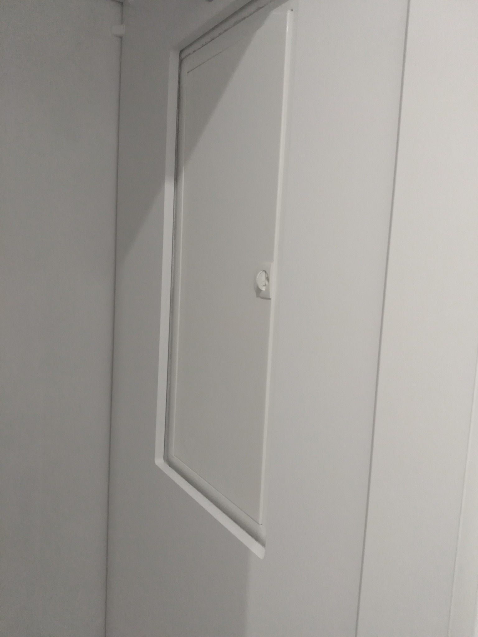 Biała klapa rewizyjna z zamkiem wbudowana w ścianę, widok z boku.