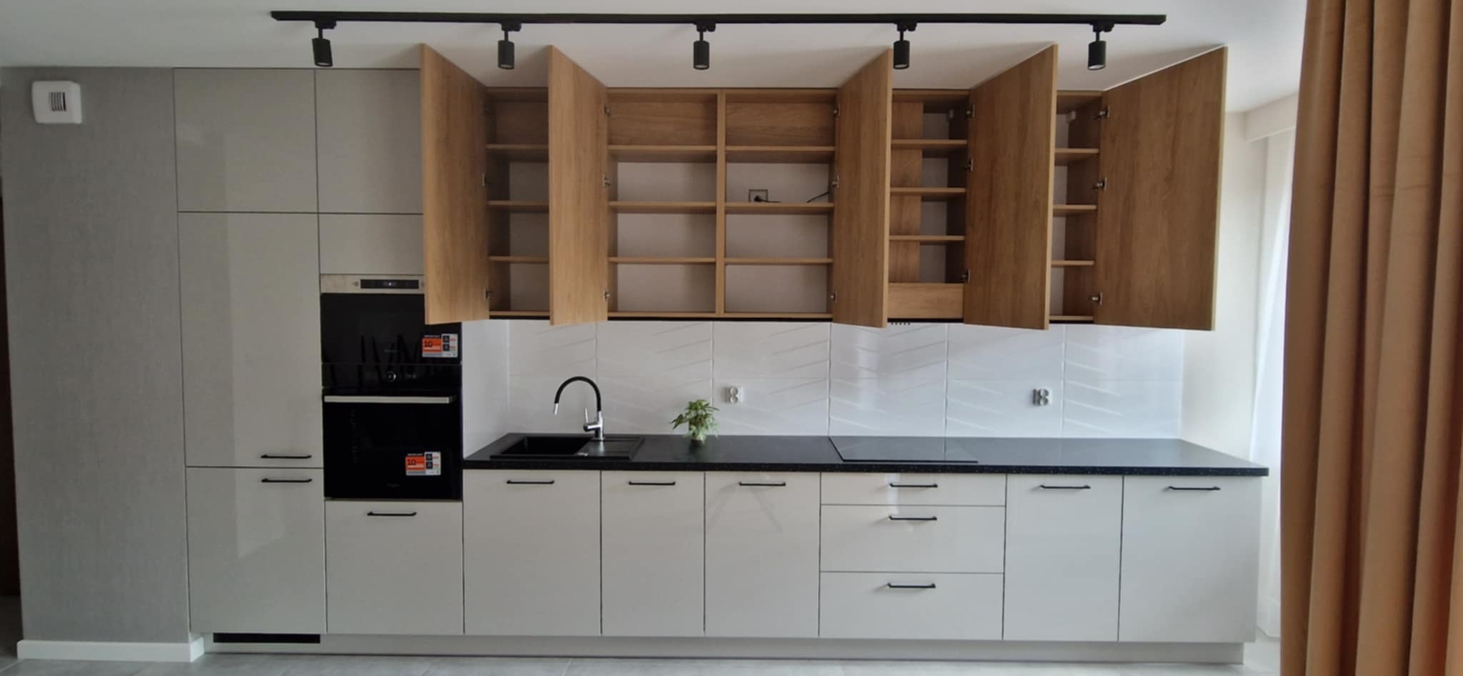 Nowoczesna kuchnia w odcieniach szarości i drewna z otwartymi szafkami wiszącymi, czarnym blatem i minimalistycznym oświetleniem punktowym.